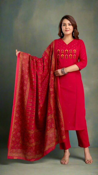 Woman in a red traditional kurta set with a patterned dupatta against a textured wall.