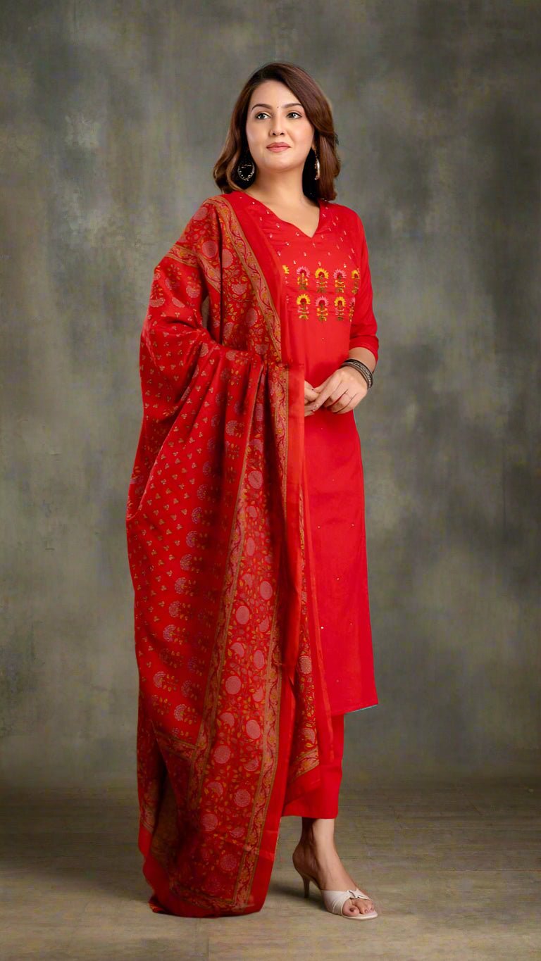 Woman in a red traditional kurta set with a matching dupatta against a textured wall.