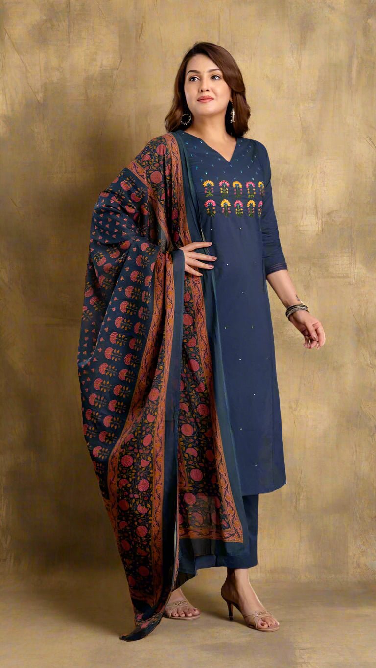 Woman wearing a navy blue kurta with a patterned dupatta, standing indoors with a plant in the background.