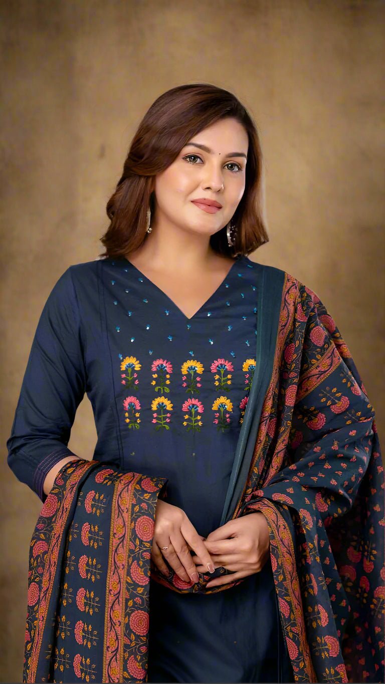 Woman wearing a blue outfit with colorful patterns, standing against a neutral background.