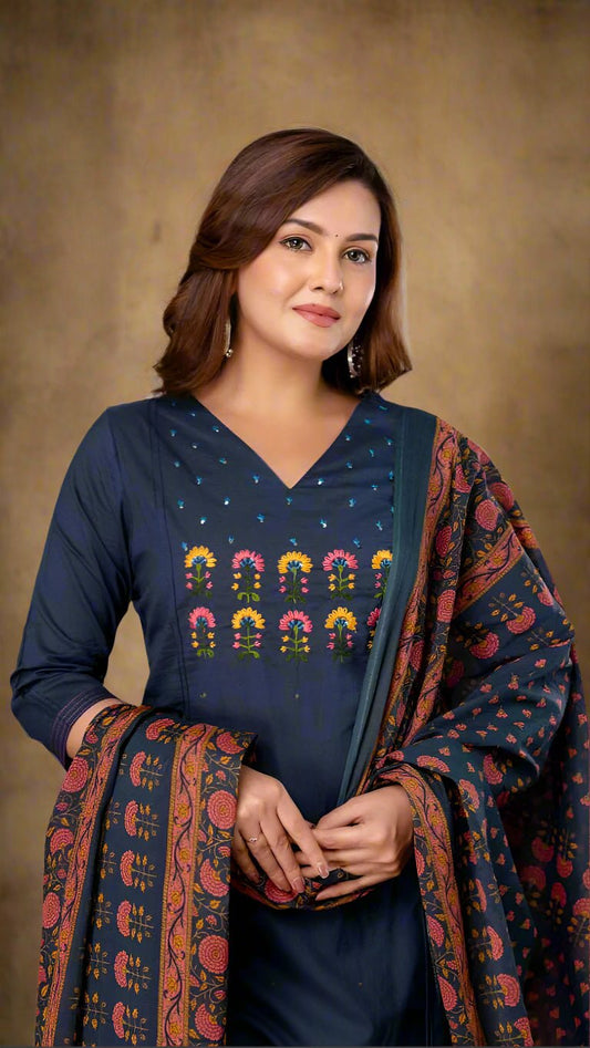 Woman wearing a blue outfit with colorful patterns, standing against a neutral background.