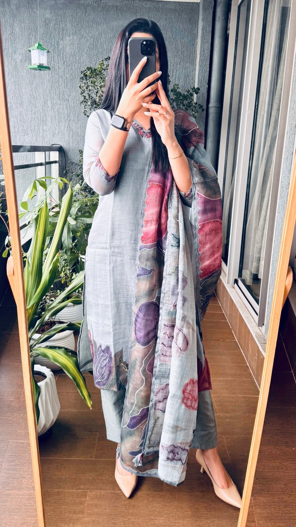 Person wearing a colorful kurti set in grey in a room with plants and a window.