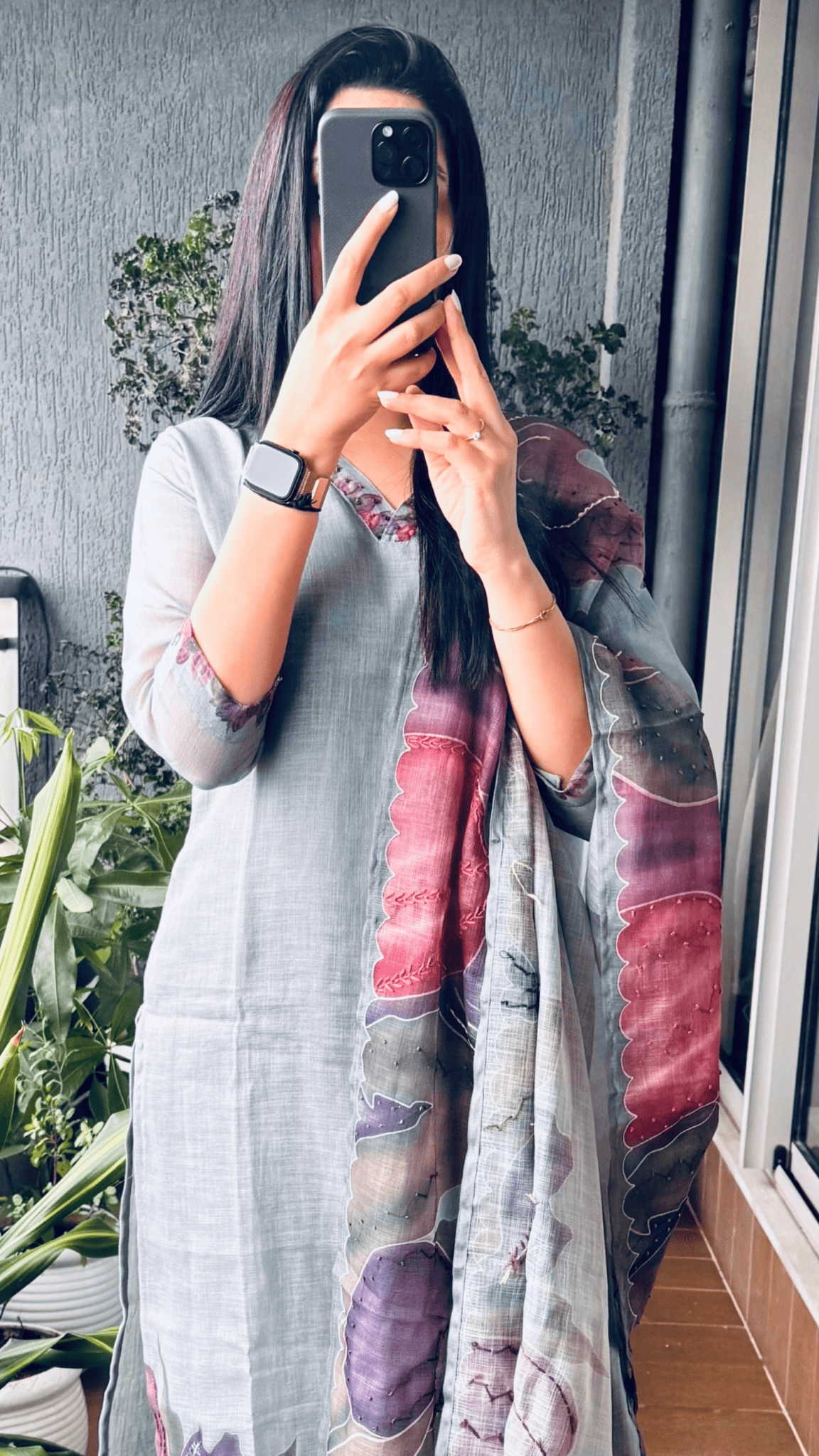 Person wearing a colorful kurta set in a room with plants and a window.