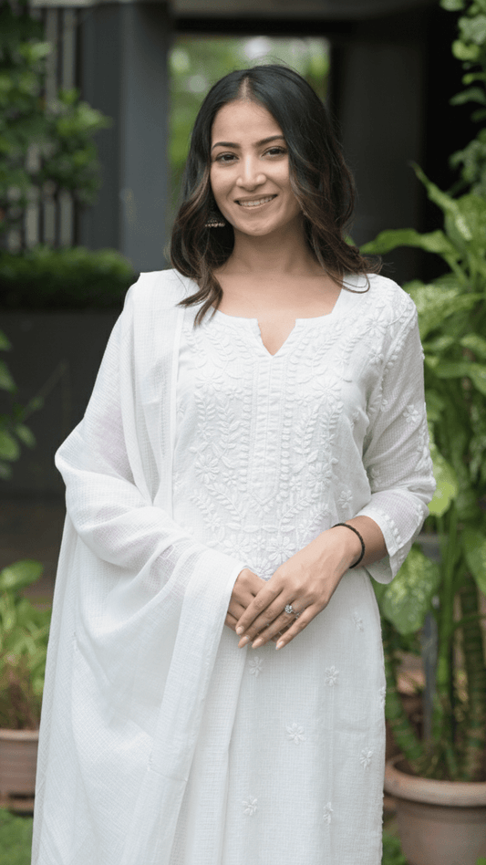 Woman in a white outfit standing outdoors with greenery in the background