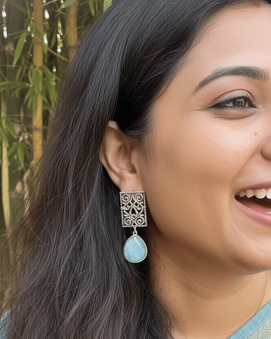 Woman wearing a silver earring with a blue gemstone outdoors