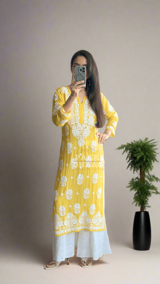 Person wearing a yellow chikankari hand embroidered kurta dress standing in front of a mirror with plants around.