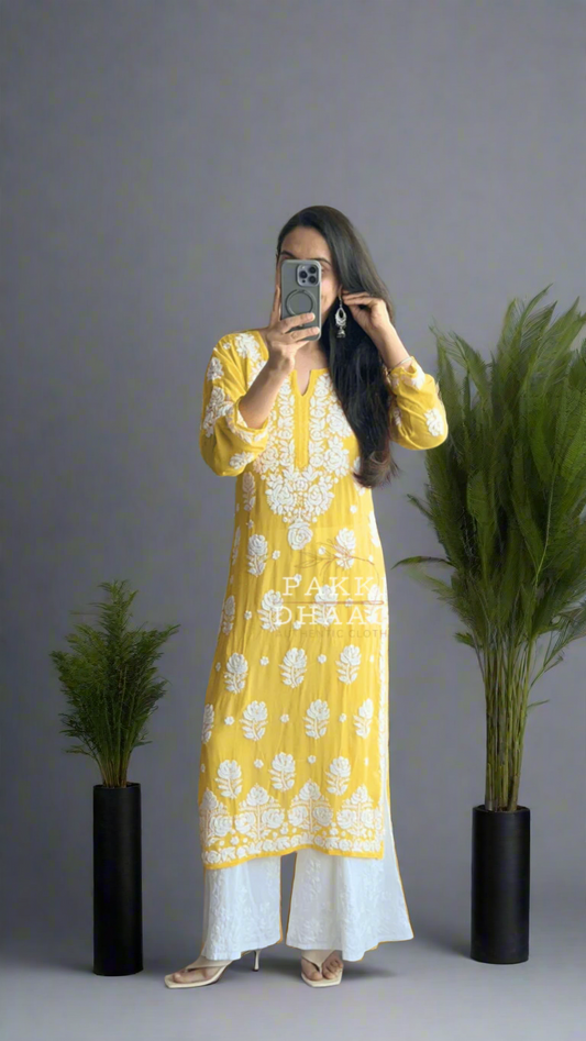 Person wearing a yellow and white chikankari kurta standing in front of a mirror with plants around.