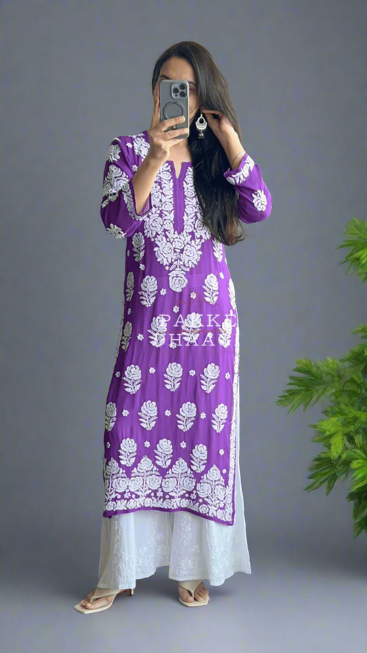 Person wearing a purple chikankari dress with white embroidery standing in front of a mirror with plants in the background