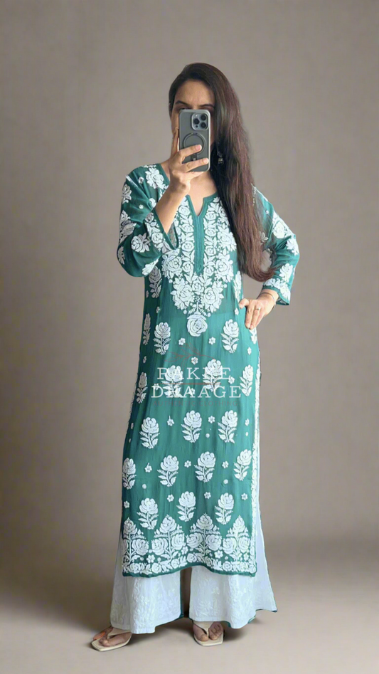 Person wearing a green and white floral chikankari suit standing in front of a mirror with plants around.