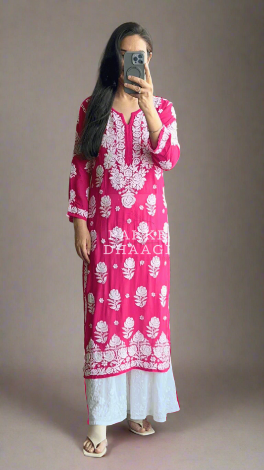 Person wearing a pink and white patterned chikankari kurti standing in front of a mirror with plants around.