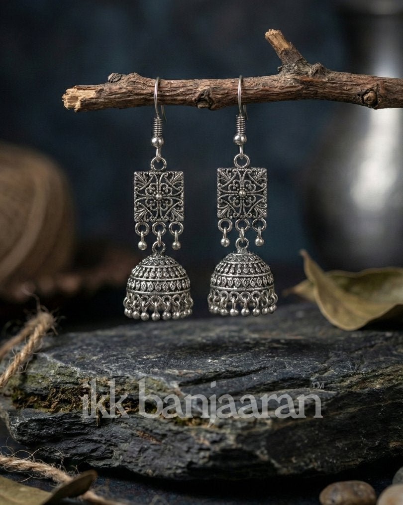 Pair of art silver earrings on a branch with 'ikka banjaraan' branding.