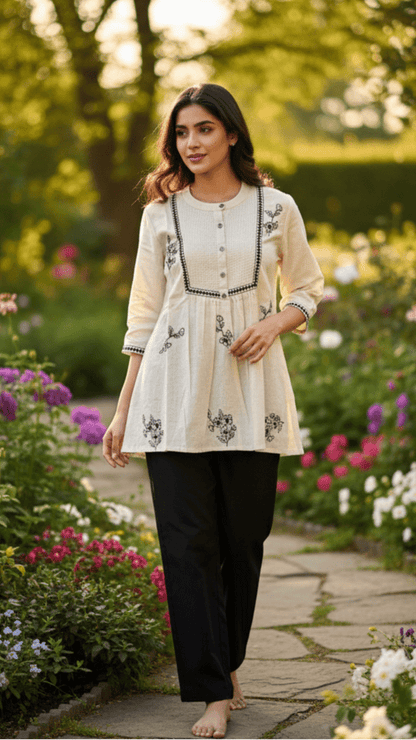 Woman standing in a garden with flowers and trees in the background, wearing embroidered short kurti by Pakke Dhaage