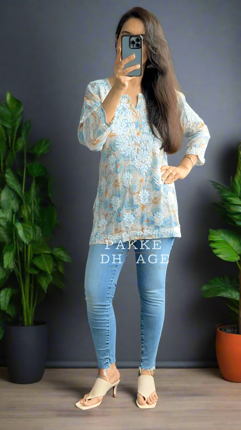 Person taking a mirror selfie wearing a blue patterned chikankari top and light blue jeans in a room with plants.