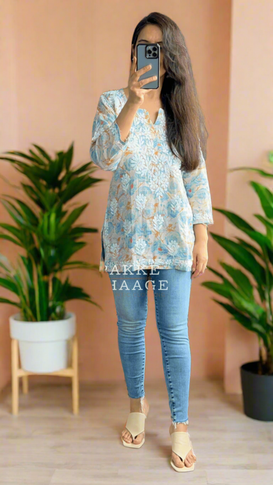 Person taking a mirror selfie wearing a floral blue chikankari top and blue jeans in a room with plants.