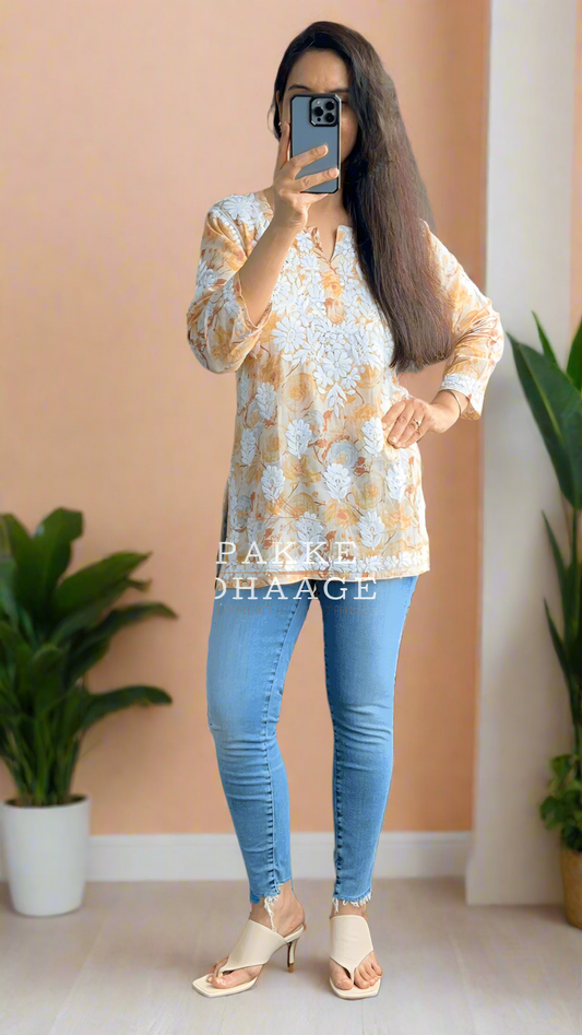 Person wearing a patterned chikankari top and blue jeans in a room with plants.
