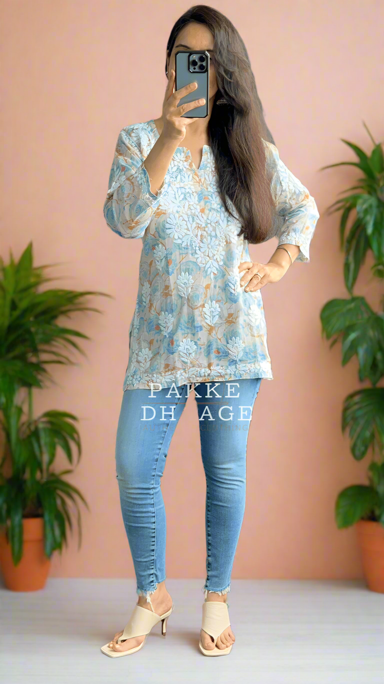 Person taking a mirror selfie wearing a blue patterned chikankari top and light blue jeans in a room with plants.