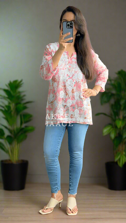 Person wearing a floral pink chikankari top and blue jeans in a room with plants.