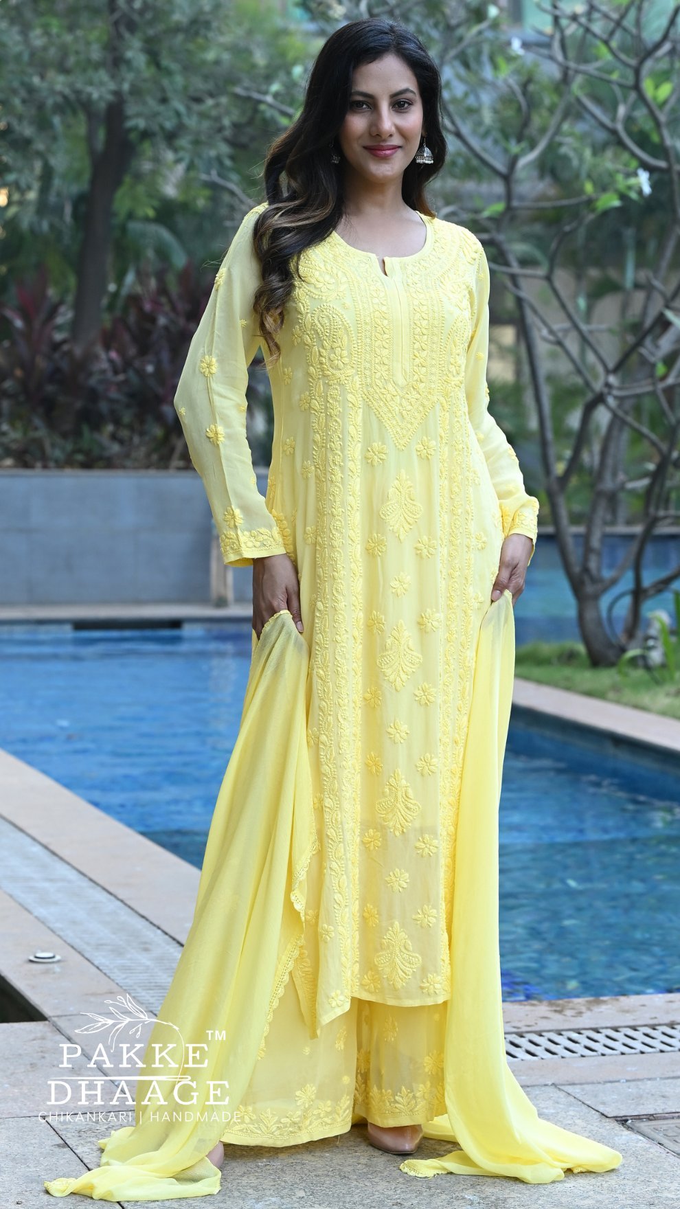 Woman in a yellow chikankari viscose outfit standing by a pool with greenery in the background