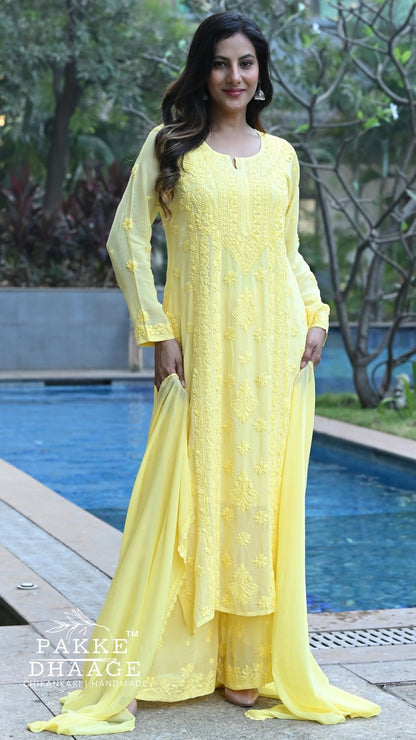 Woman in a yellow chikankari viscose outfit standing by a pool with greenery in the background