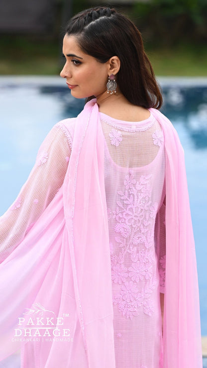 A woman wearing a light pink traditional outfit with floral chikankari and a matching sheer dupatta, photographed outdoors near a pool. The brand name 'PAKKE DHAAGE' is visible as a watermark in the lower-left corner.