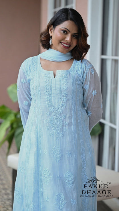 A woman wearing a light blue embroidered chikankari kurta with a matching dupatta, standing in front of a window. The brand name 'PAKKE DHAAGE' is visible as a watermark in the bottom right corner.