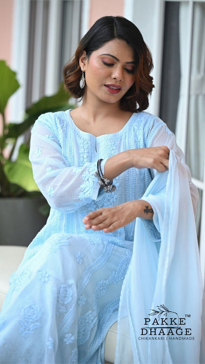 A woman wearing a light blue embroidered chikankari outfit with a matching sheer dupatta, posed in an indoor setting. The brand logo 'PAKKE DHAAGE' is visible in the bottom right corner.