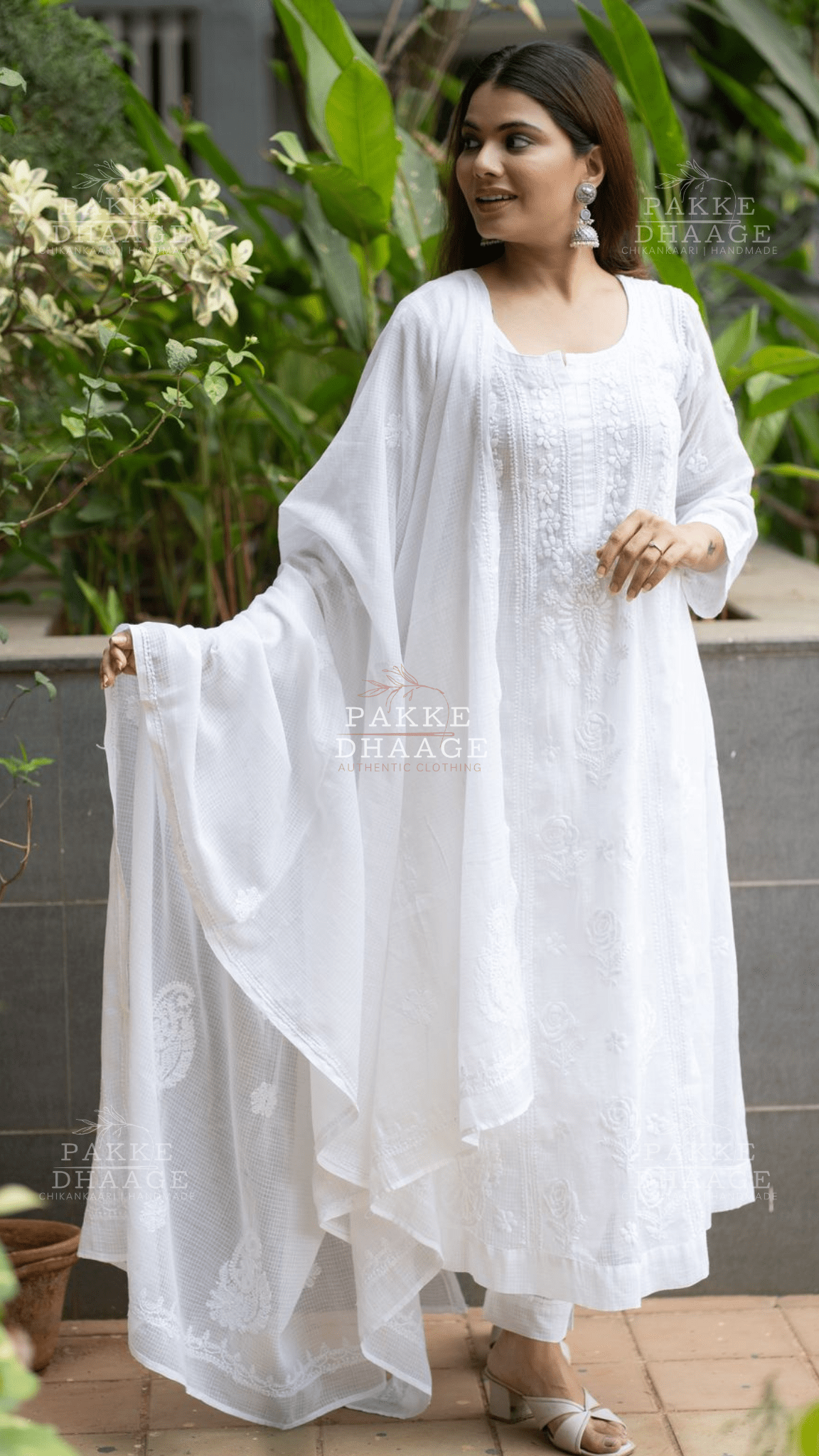 Woman wearing a white chikankari anarkali suit with a flowing drape in an outdoor setting.