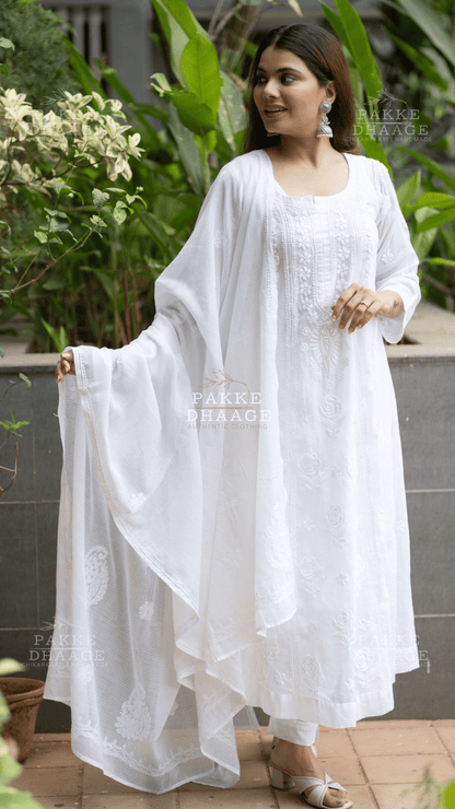 Woman wearing a white chikankari anarkali suit with a flowing drape in an outdoor setting.