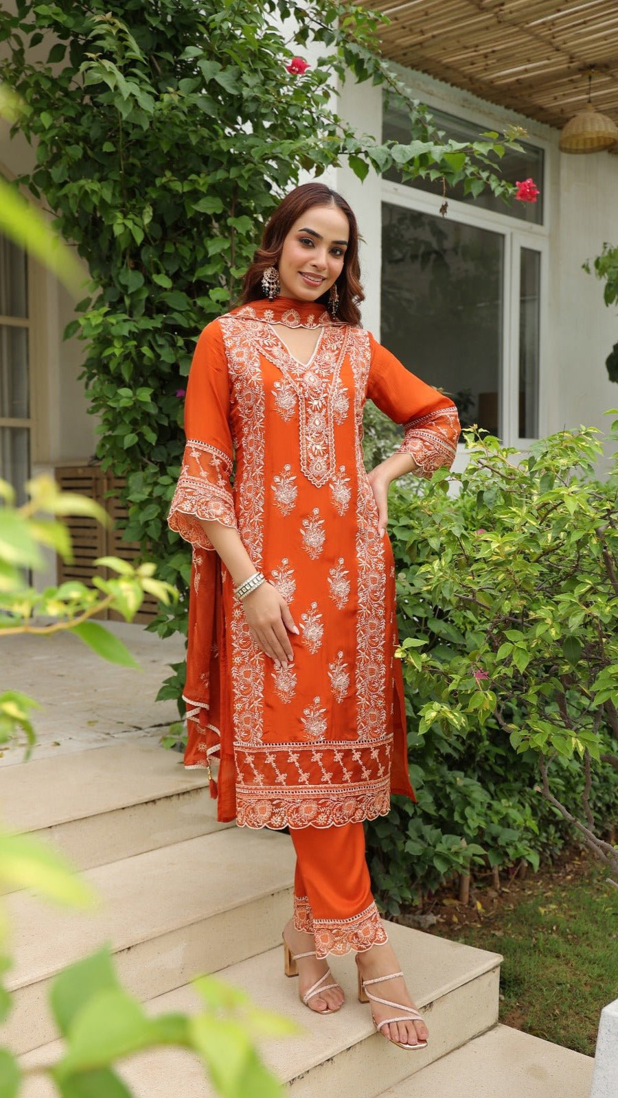 Woman in an orange embroidered outfit standing on steps outdoors.