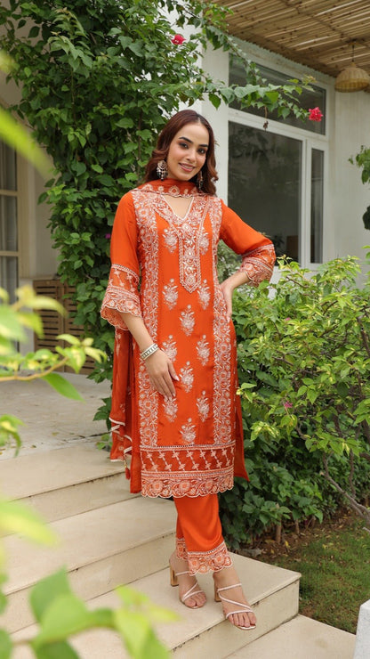 Woman in an orange embroidered outfit standing on steps outdoors.