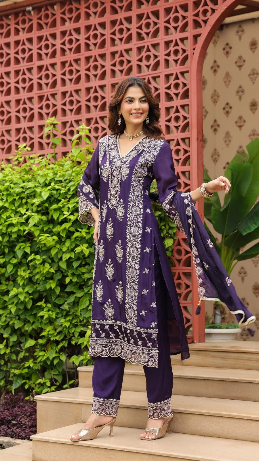 Woman in a purple traditional outfit standing outdoors with decorative elements in the background
