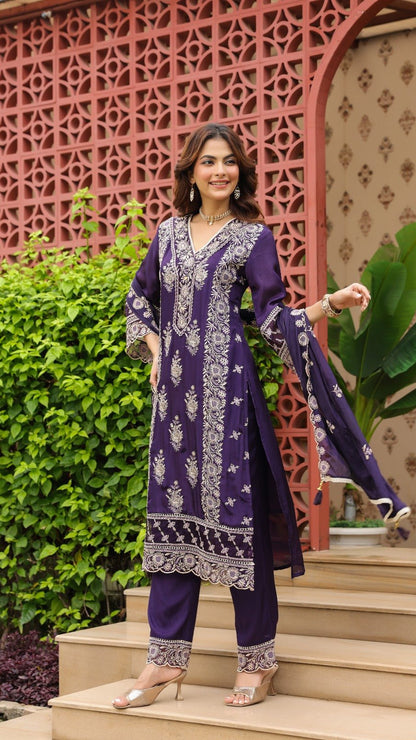 Woman in a purple traditional outfit standing outdoors with decorative elements in the background