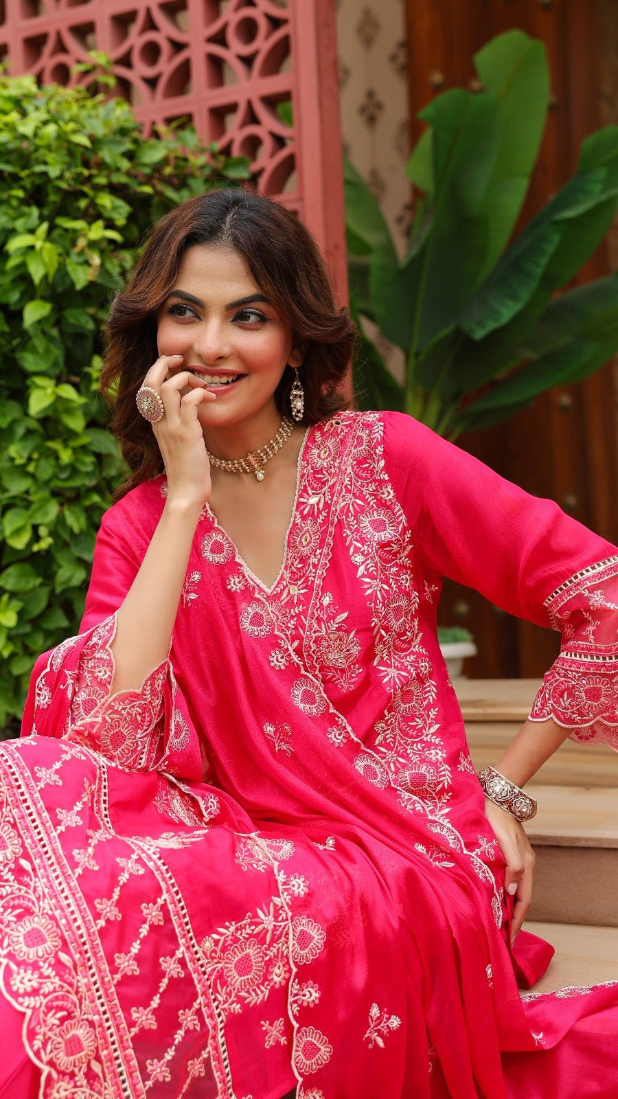 Woman in a pink traditional outfit with white embroidery sitting outdoors.