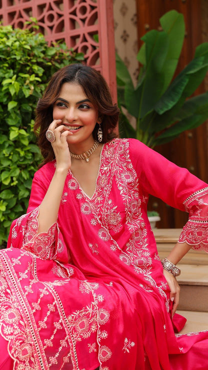 Woman in a pink traditional outfit with white embroidery sitting outdoors.
