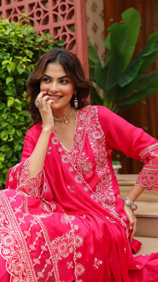 Woman in a pink traditional outfit with white embroidery sitting outdoors.