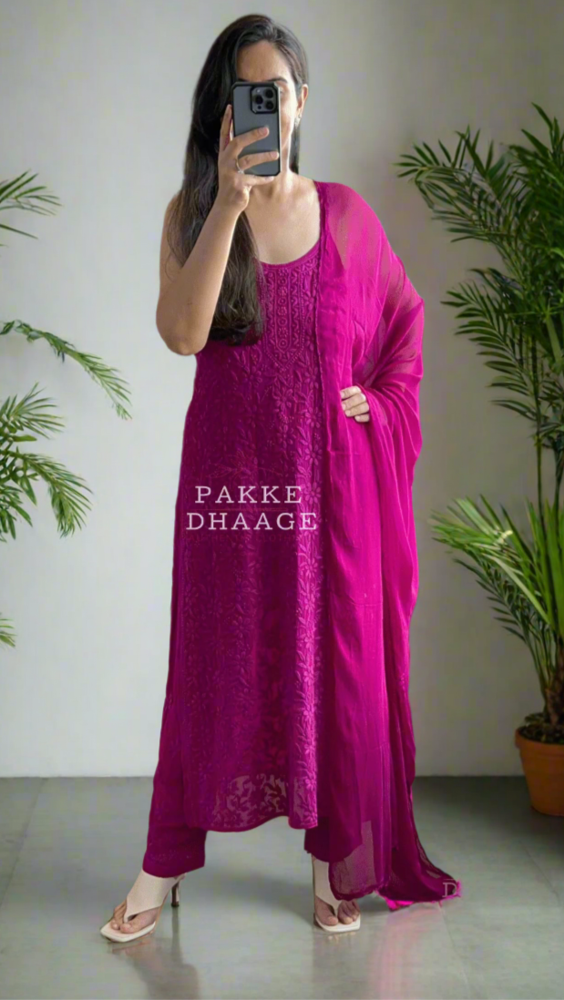 Person wearing a bright pink traditional outfit standing in front of a mirror with plants around.