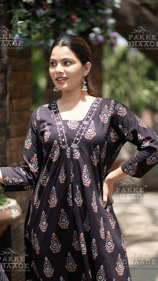 Woman wearing a black patterned dress with 'Pakke Dhaage' branding in the background.