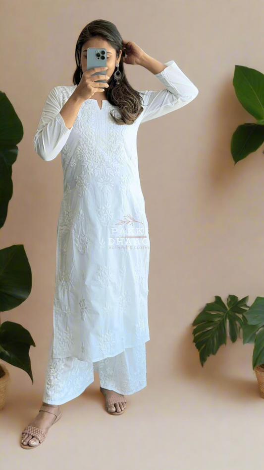 Person wearing a white chikankari outfit standing in front of a mirror with plants in the background.