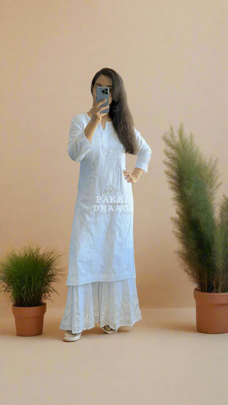 Woman in a white Chikankari outfit standing in a room with plants around