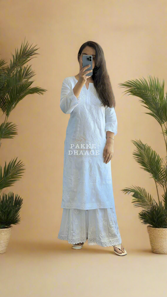Person wearing a white chikankari outfit taking a mirror selfie with plants in the background