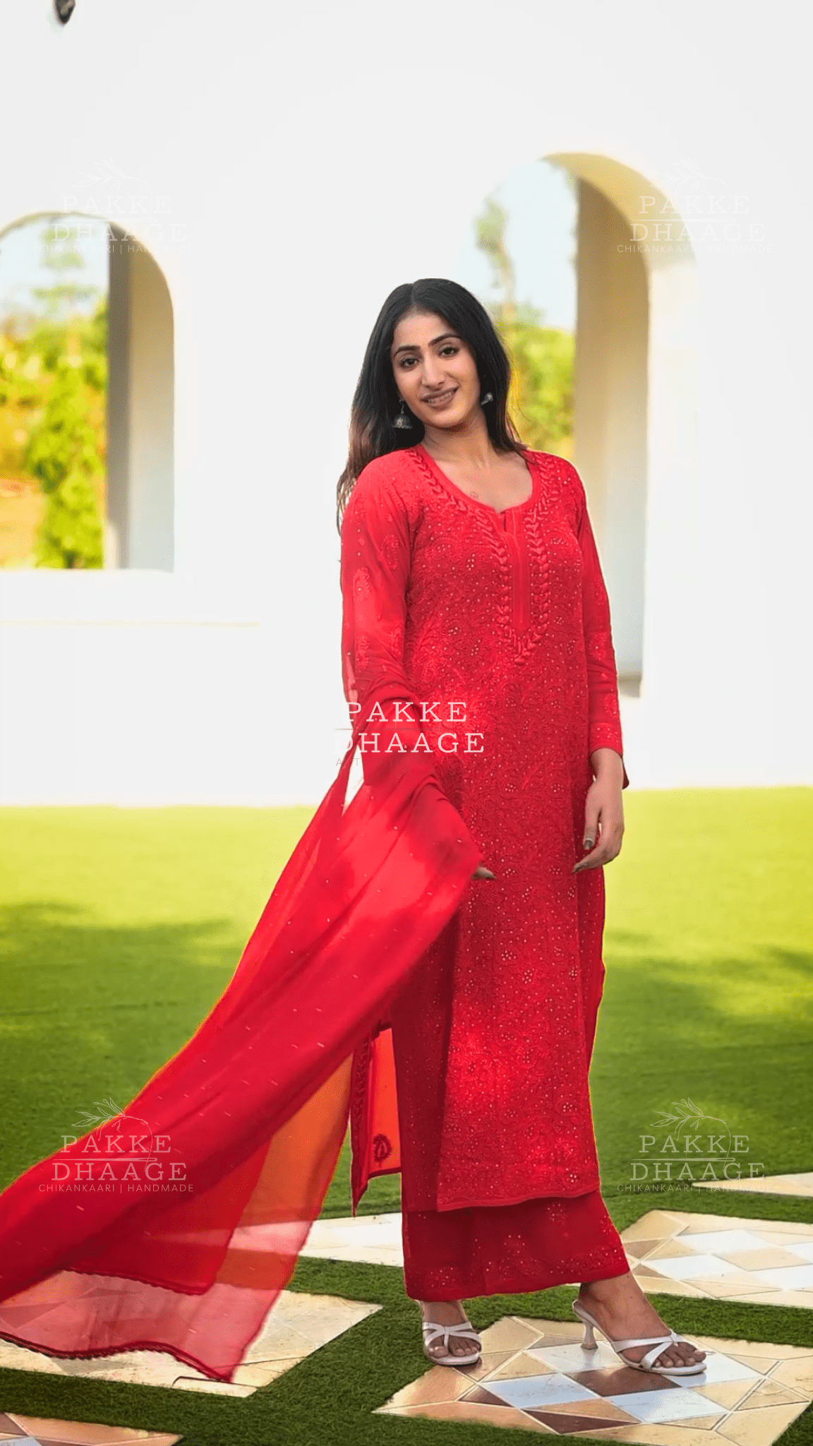 Woman in a red hand-embroidered viscose suit standing outdoors with greenery in the background