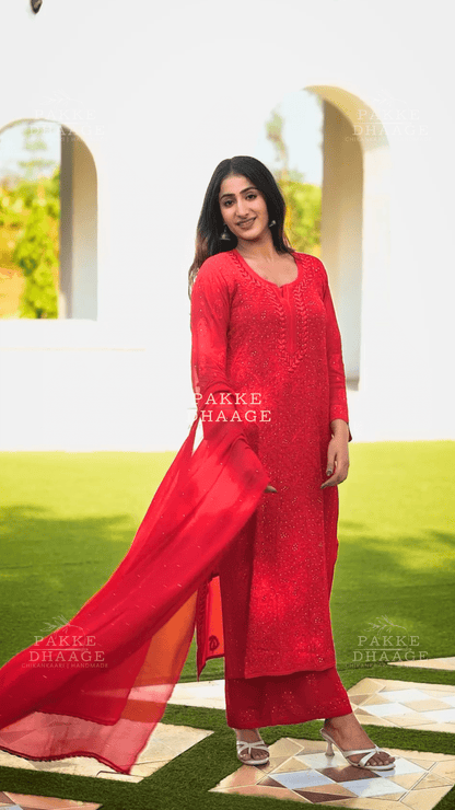 Woman in a red hand-embroidered viscose suit standing outdoors with greenery in the background