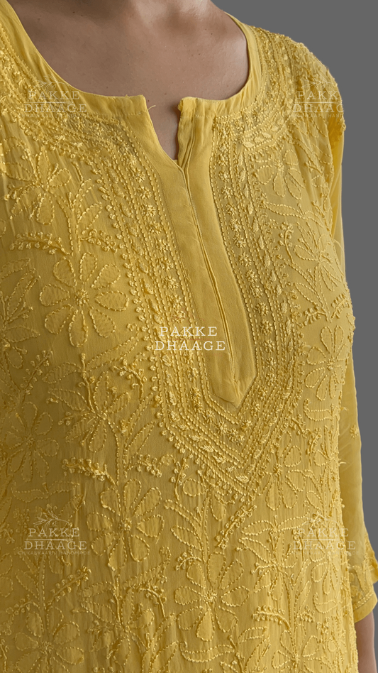 Yellow embroidered dress with intricate chikankari patterns on a blurred background