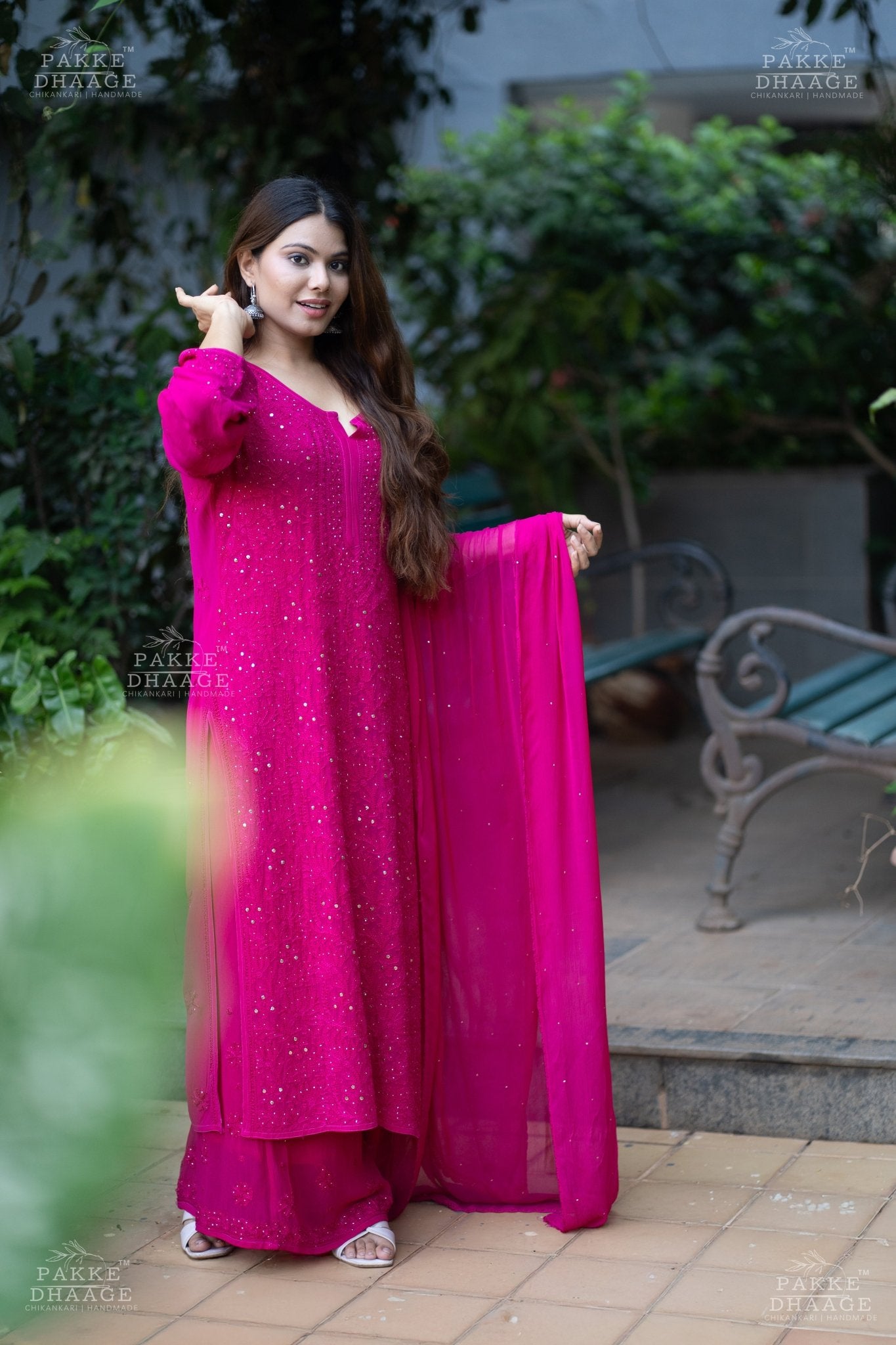 Woman in a pink hand-embroidered chikankari suit standing outdoors with greenery in the background