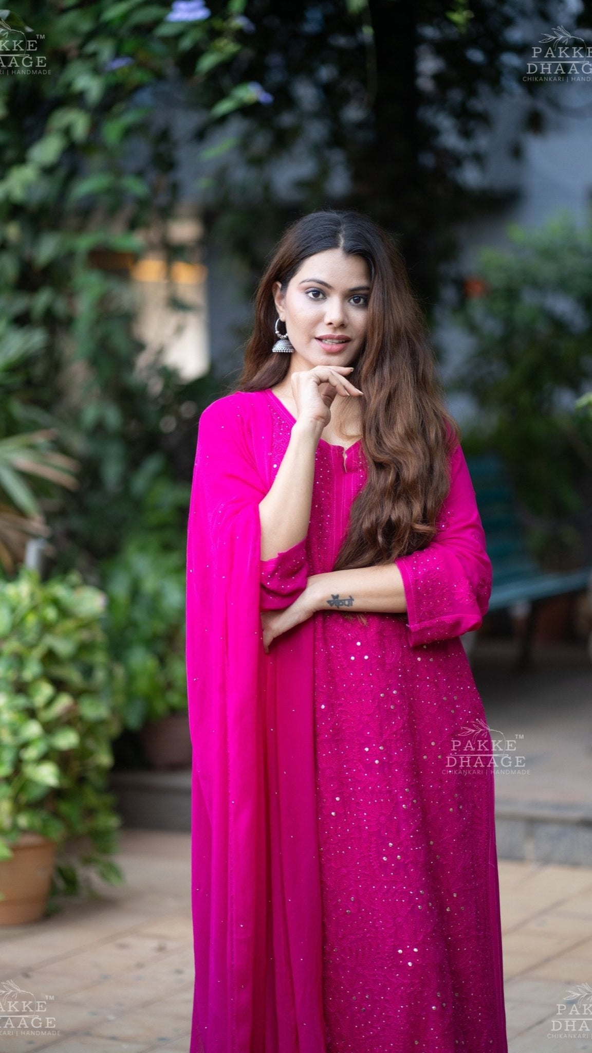 Woman in a bright pink chikankari set with a matching dupatta, standing outdoors.