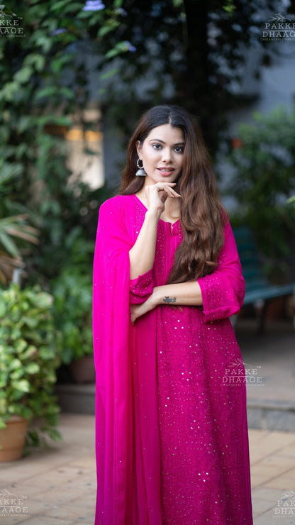 Woman in a bright pink chikankari set with a matching dupatta, standing outdoors.