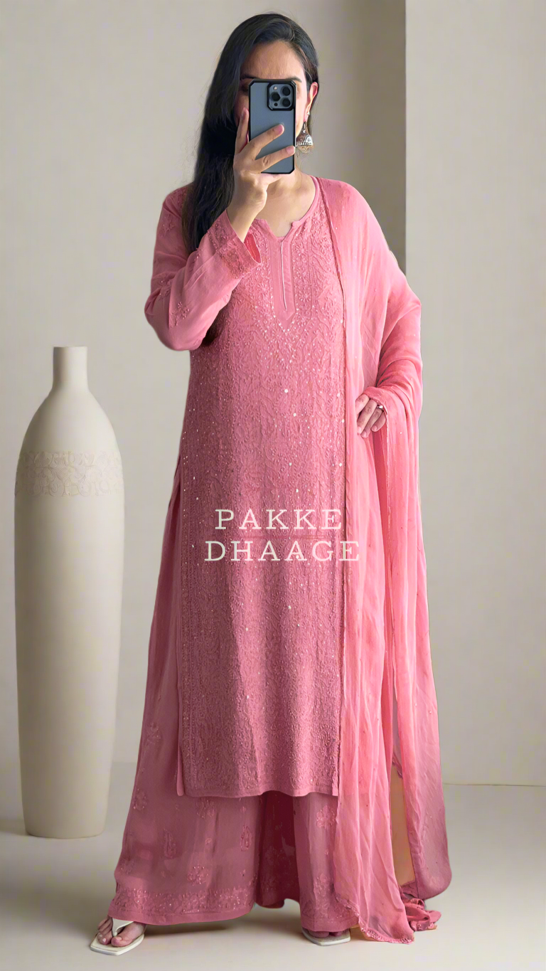 Person wearing a pink outfit standing in front of a mirror with plants around.