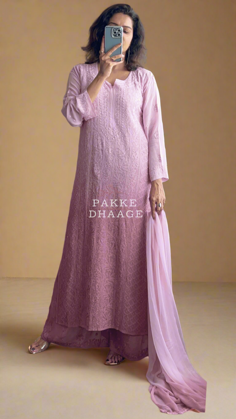 Woman in a pink dress standing in front of a mirror with plants around.