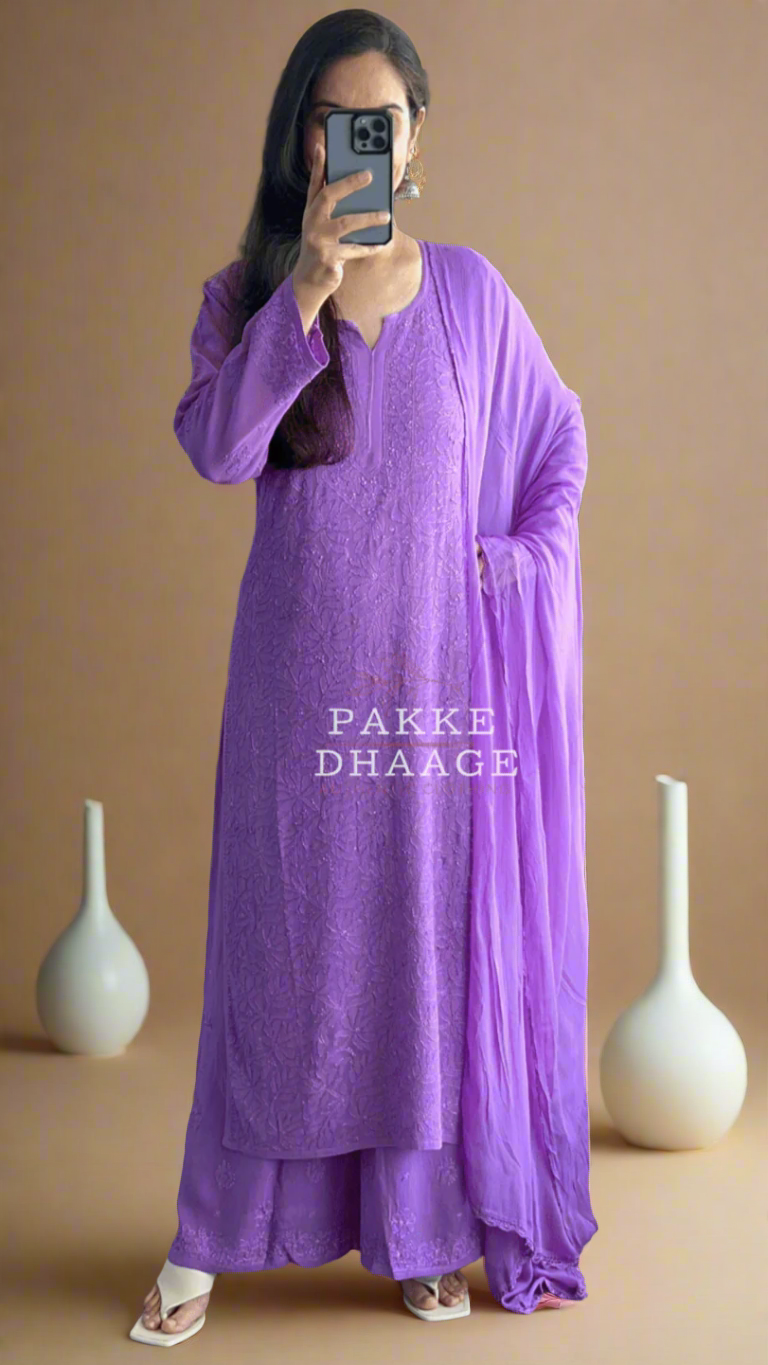 Person wearing a purple chikankari hand embroidered kurti set, with 'PAKKE DHAAGE' branding, standing indoors.