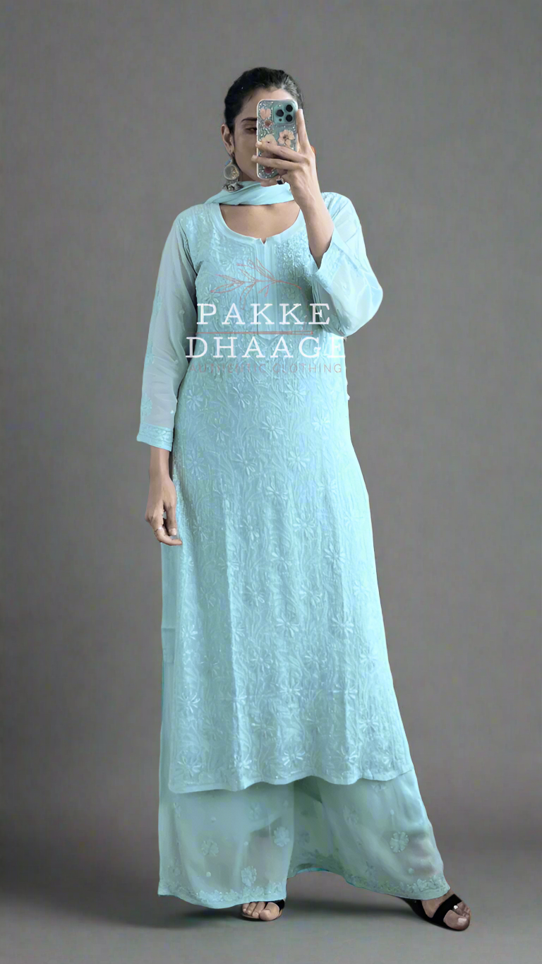 Person wearing a light mint coloured handmade chikankari kurti set, with matching dupatta, standing with plants around.